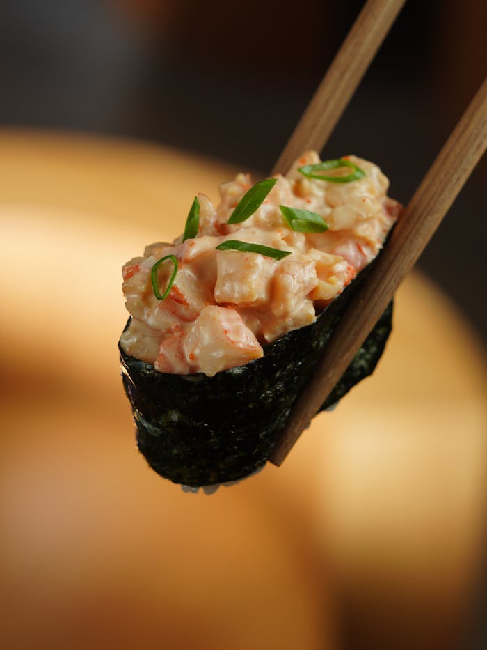 Close-up of a spicy tuna gunkan sushi held by chopsticks in a vertical shot.
